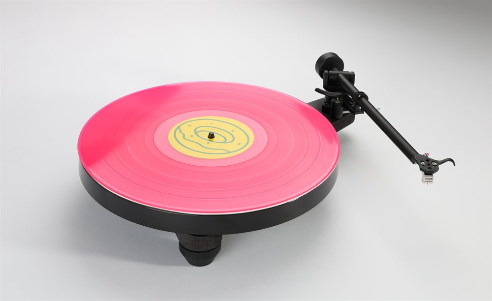 The Rega Replay in matt black, three-quarter view from above, a pink record on the platter and the RB110 tonearm on its rest.